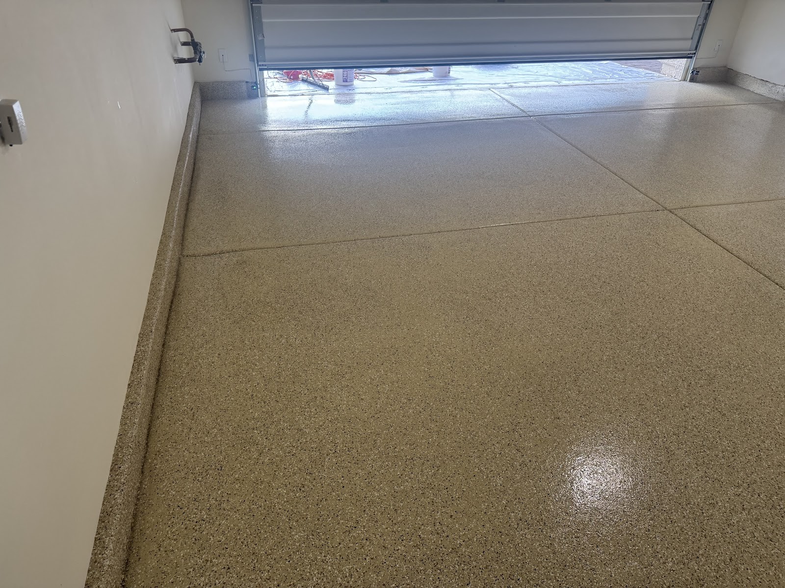 Close-up of a glossy speckled epoxy garage floor near an open garage door
